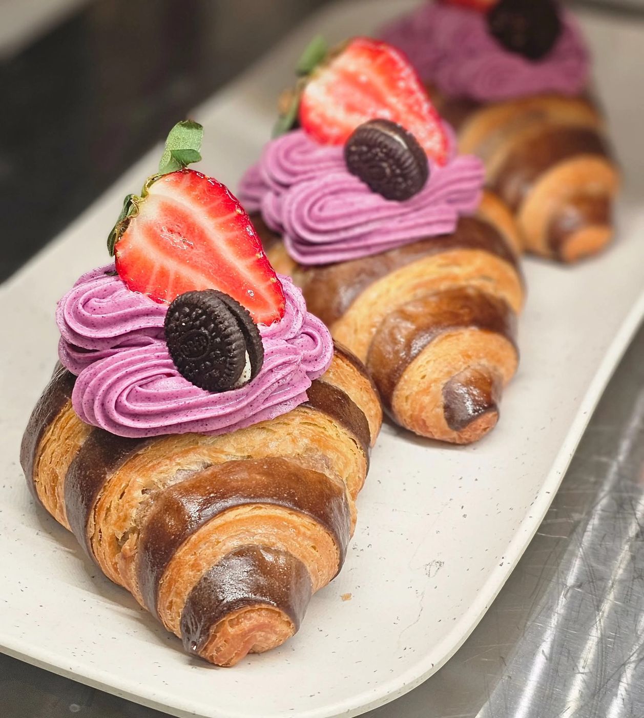 Chocolate-striped croissants crowned with blueberry cream, fresh strawberry, and a mini cookie