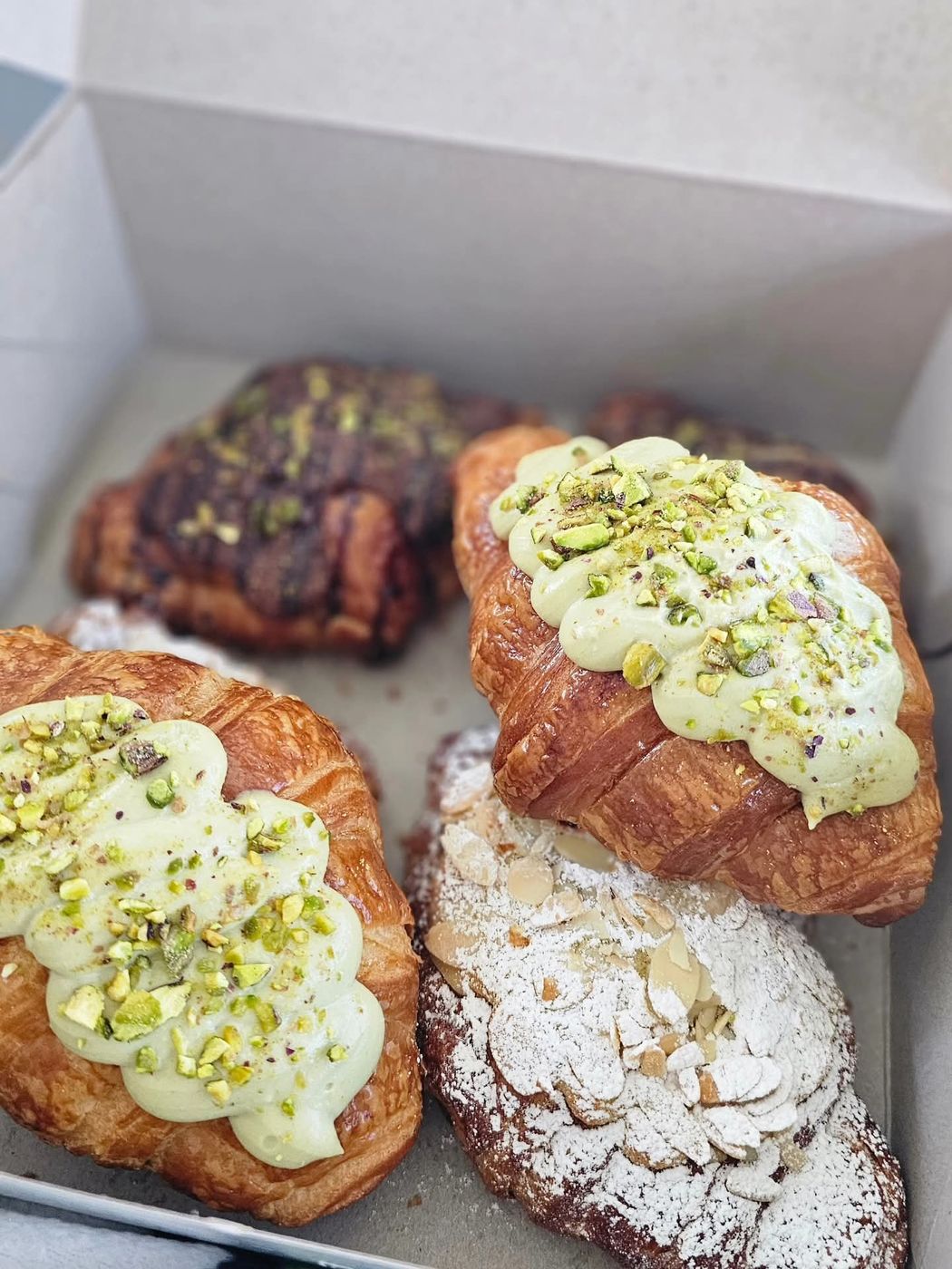 Pistachio cream croissants dusted with crushed pistachios, boxed to go